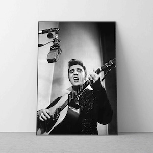 May include: Black and white photo of Elvis Presley singing into a microphone while playing an acoustic guitar.