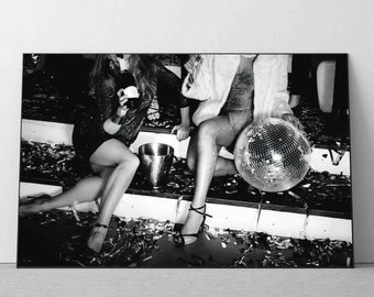 May include: Two people in a party setting, one holding a champagne glass and the other sitting with a disco ball. The floor is covered in confetti.