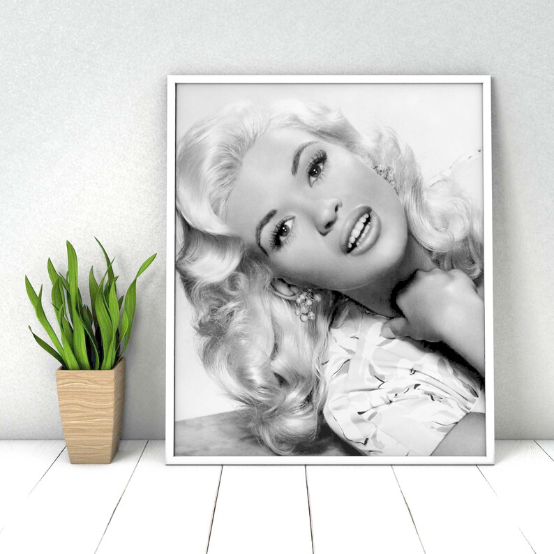 K&ouml;nnte beinhalten: Schwarzwei&szlig;-Portr&auml;tfotografie einer Frau mit blonden Haaren. Sie tr&auml;gt eine wei&szlig;e Bluse mit Blumenmuster und l&auml;chelt leicht.