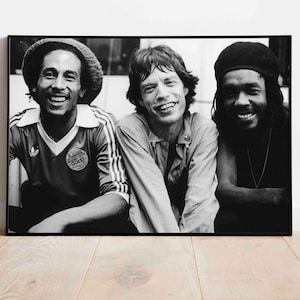 Puede incluir: Foto en blanco y negro de tres hombres sonriendo. El hombre de la izquierda lleva un sombrero y una camiseta de fútbol. El hombre del centro lleva una camisa abotonada. El hombre de la derecha lleva una boina y un collar.