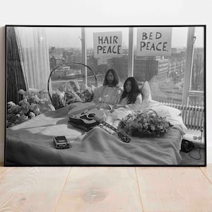 May include: Black and white photo of John Lennon and Yoko Ono in bed, holding signs that read "Hair Peace" and "Bed Peace".