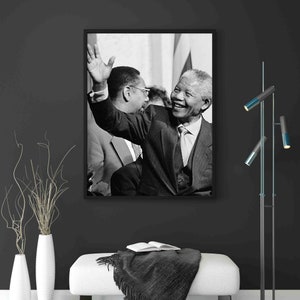 Puede incluir: Fotograf&iacute;a en blanco y negro de Nelson Mandela sonriendo y saludando. Lleva un traje y una corbata. La foto est&aacute; enmarcada en un marco negro.