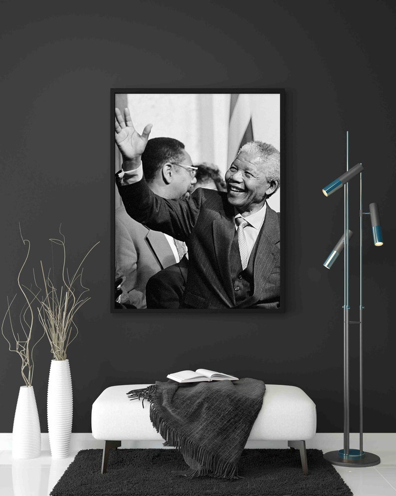 Puede incluir: Fotograf&iacute;a en blanco y negro de Nelson Mandela sonriendo y saludando. Lleva un traje y una corbata. La foto est&aacute; enmarcada en un marco negro.