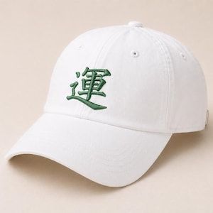 May include: White baseball cap with a curved brim. The cap features a green embroidered Japanese character on the front. The cap has a button on top and an adjustable strap at the back. A casual accessory.