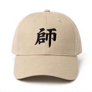 May include: A beige baseball cap featuring black embroidered Chinese characters on the front panel. The cap has a structured crown, a curved brim, and stitched eyelets for ventilation, providing a classic look with a neutral color palette.