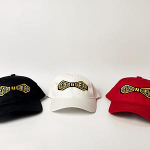 May include: Three baseball caps with a black, white, and red color scheme. Each cap features a yellow and black bow tie design with the text "ER SIR HEAD" embroidered on it.
