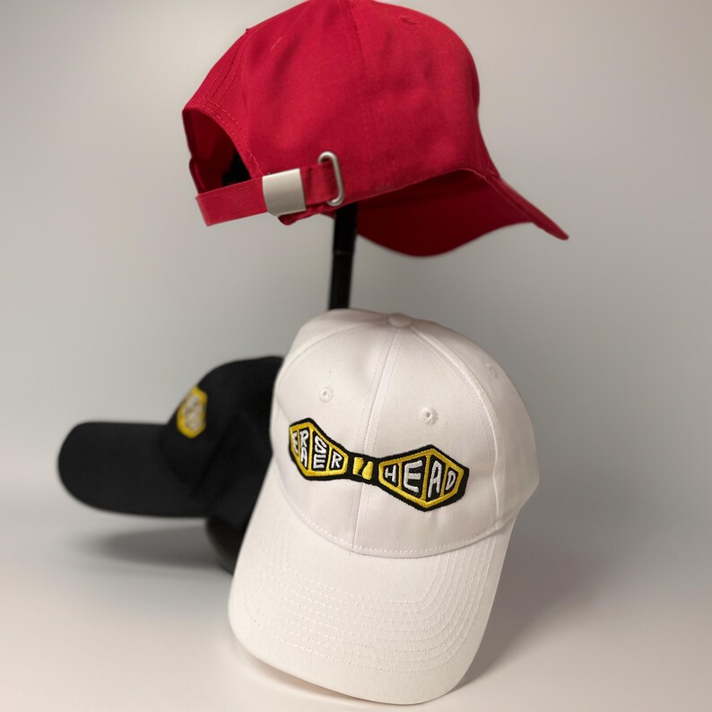May include: Three baseball caps, one red, one white with a yellow and black "Fresh Head" logo, and one black.