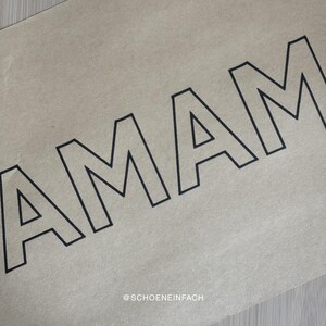 Puede incluir: Primer plano de un papel beige con la palabra "AMAM" en letras negras y en negrita. La esquina inferior derecha del papel tiene el texto "@SCHOENEINFACH" en una fuente m&aacute;s peque&ntilde;a.