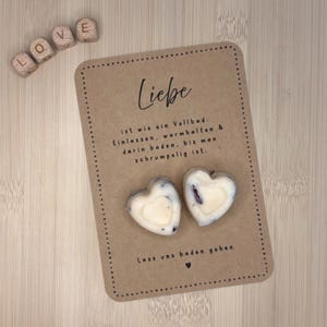 Könnte beinhalten: Eine Karte aus Kraftpapier mit dem Wort "Liebe" und Text auf Deutsch, zusammen mit zwei herzförmigen Seifen. Holzbuchstabenblöcke buchstabieren "LOVE".