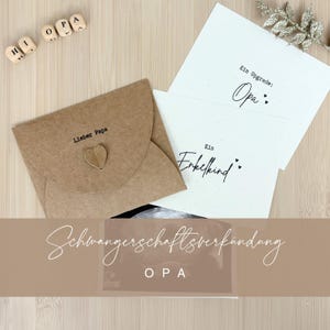 Könnte beinhalten: Eine Auswahl an Schwangerschaftsankündigungskarten und Holzblöcken mit der Aufschrift "OPA". Die Karten sind weiß und beige, mit deutschem Text. Eine Karte lautet "Ein Enkelkind", eine andere "Ein Upgrade: Opa:". Ein brauner Umschlag mit einem Herz ist ebenfalls vorhanden.