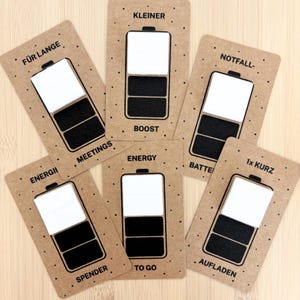 Könnte beinhalten: Eine Sammlung brauner Papierkarten mit einem Batteriedesign. Jede Karte hat eine andere Textbezeichnung, darunter "Meetings", "Energy" und "Boost". Die Batterie-Grafik zeigt unterschiedliche Ladestände mit schwarzen und weißen Abschnitten.