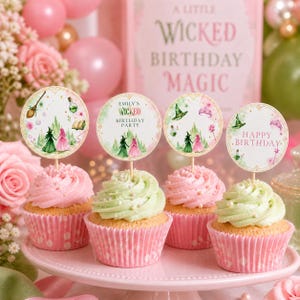 May include: Cupcakes with pink and green frosting, topped with decorative toppers. The toppers feature a witch theme with text that reads "Emily's Wicked Birthday Party" and "Happy Birthday". The cupcakes sit on a pink cake stand.
