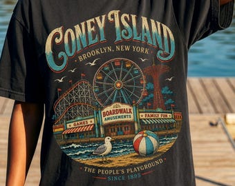 May include: Black t-shirt featuring a Coney Island design. The graphic includes a Ferris wheel, roller coaster, and the text "Coney Island Brooklyn, New York". A seagull and a beach ball are also depicted. The shirt is made of a soft material.