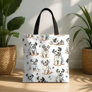 May include: White tote bag featuring a repeating pattern of adorable Dalmatian puppies with black spots and paw prints. The bag has black handles and is suitable for carrying various items. The design is playful and suitable for dog lovers.