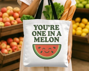May include: White tote bag with black handles featuring the text "YOU'RE ONE IN A MELON" in green, with a smiling watermelon slice graphic. The bag is filled with lettuce and baguettes.