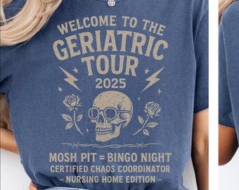 May include: A blue t-shirt with the text "WELCOME TO THE GERIATRIC TOUR 2025" in a distressed font. The design includes a skull wearing glasses, lightning bolts, and roses. Additional text reads "MOSH PIT = BINGO NIGHT, CERTIFIED CHAOS COORDINATOR - NURSING HOME EDITION".