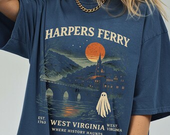 May include: A navy blue t-shirt featuring a graphic of Harpers Ferry, West Virginia, with a bridge, buildings, and a ghost. The text reads "HARPERS FERRY" above the graphic and "WEST VIRGINIA WHERE HISTORY HAUNTS" below.