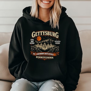 May include: A black hooded sweatshirt featuring a graphic print with the text GETTYSBURG, CIVIL WAR HISTORY, BATTLEFIELD LEGENDS, EST. LEGENDARY BATTLEFIELD, and PENNSYLVANIA, depicting cannons, figures, and a moonlit night scene.