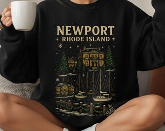 May include: Black sweatshirt with a Newport, Rhode Island graphic. The design features a detailed illustration of buildings, sailboats, and trees, with the text "NEWPORT RHODE ISLAND" in a gold color. The sweatshirt has a crew neck.