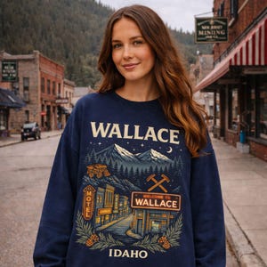 May include: Navy blue sweatshirt with a graphic of Wallace, Idaho, featuring a mountain scene, a mining truck, and a street view with the text "WELCOME TO WALLACE" and "IDAHO".