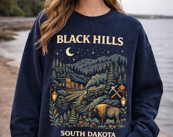 May include: Navy blue sweatshirt with a graphic featuring the text "BLACK HILLS SOUTH DAKOTA". The design includes a train, bison, trees, and a night sky with a crescent moon and stars.