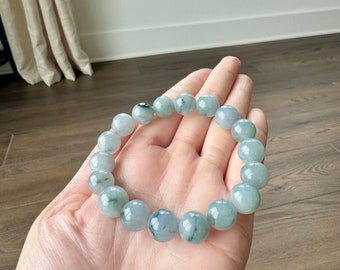 Pode incluir: Um bracelete de jade com contas verdes e brancas. O bracelete é feito de jade natural e tem um acabamento polido.