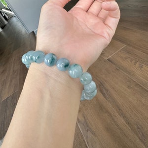 May include: A jade bracelet with light green and dark green beads. The bracelet is on a person's wrist.