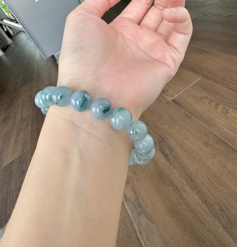May include: A jade bracelet with light green and dark green beads. The bracelet is on a person's wrist.
