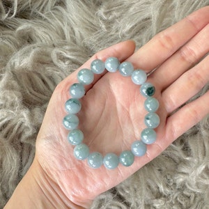 May include: A jade bracelet with light green and white beads. The bracelet is made of natural jade and has a smooth, polished finish.