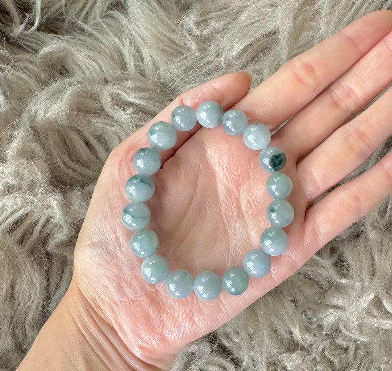 May include: A jade bracelet with light green and white beads. The bracelet is made of natural jade and has a smooth, polished finish.