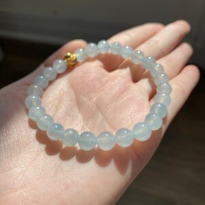 K&ouml;nnte beinhalten: Ein hellblaues Edelstein-Armband mit einem goldenen Verschluss. Das Armband besteht aus runden Perlen und ist etwa 18 cm lang.