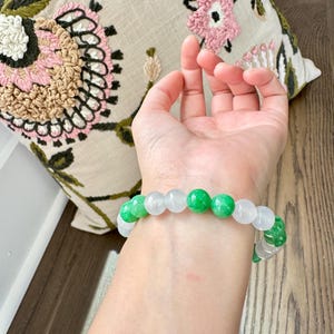 May include: A bracelet made of white and green jade beads. The bracelet is on a person's wrist.
