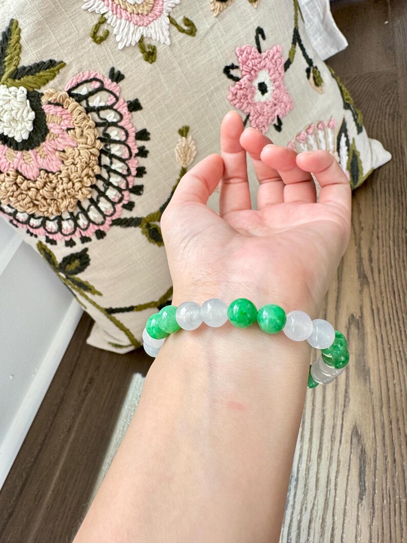 May include: A bracelet made of white and green jade beads. The bracelet is on a person's wrist.