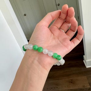May include: A bracelet made of white and green jade beads. The bracelet is on a person's wrist.