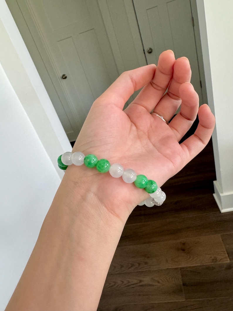 May include: A bracelet made of white and green jade beads. The bracelet is on a person's wrist.