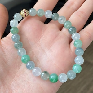Pode incluir: Um bracelete de jade&iacute;ta com um fecho de ouro e rubi. O bracelete &eacute; feito de contas redondas em tons de verde e branco.