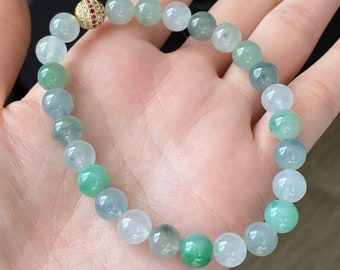 May include: A jadeite bracelet with a gold and ruby bead clasp. The bracelet is made of round beads in shades of green and white.