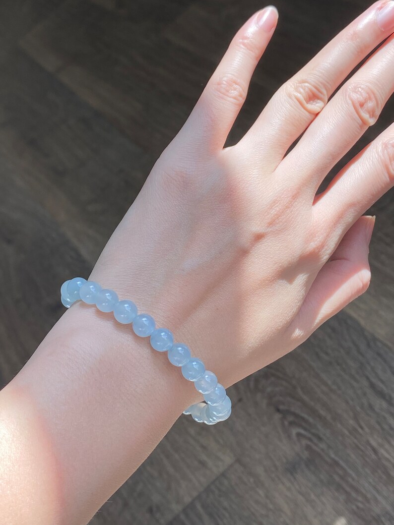 K&ouml;nnte beinhalten: Ein hellblaues Perlenarmband, das an einem Handgelenk getragen wird. Das Armband besteht aus runden, glatten Perlen.