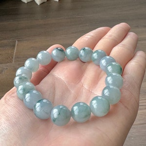 May include: A jade bracelet with light green and white beads. The bracelet is made of round beads and is approximately 18 beads long.