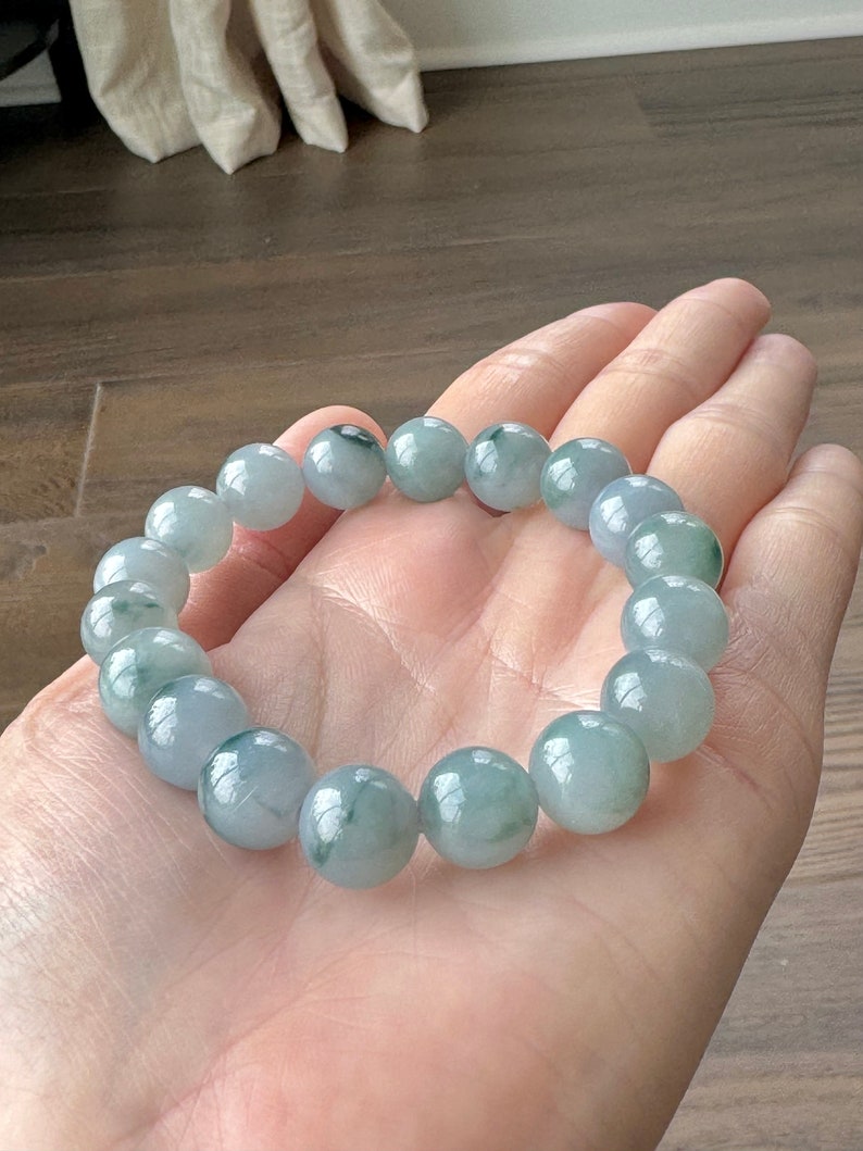 May include: A jade bracelet with light green and white beads. The bracelet is made of round beads and is approximately 18 beads long.