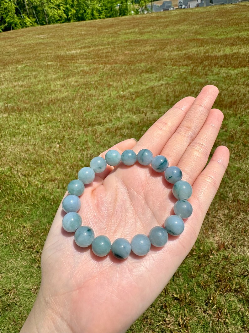 May include: A jade bracelet with green and white beads. The bracelet is made of natural jade and has a smooth, polished finish.