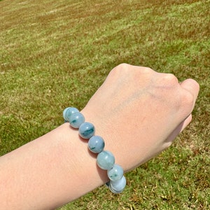 May include: A jade bracelet with green and white beads. The bracelet is on a person's wrist.