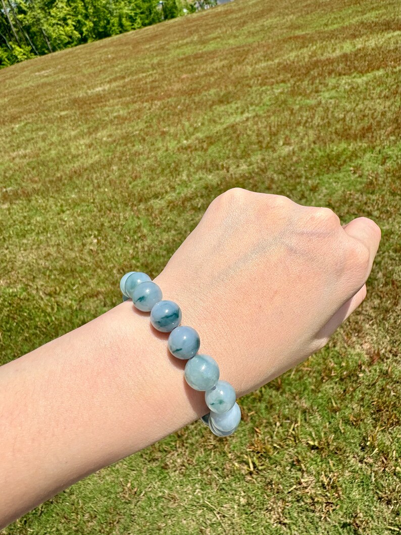 May include: A jade bracelet with green and white beads. The bracelet is on a person's wrist.