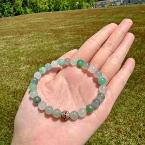 Pode incluir: Um bracelete de contas de jade verde e branco com uma conta de destaque de pedra preciosa dourada e vermelha.