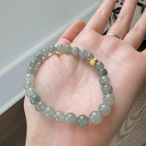 May include: A green jade beaded bracelet with a gold clasp. The bracelet is made of round beads and is approximately 7 inches in length.