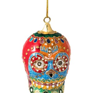 May include: A colourful, hand-painted glass bauble shaped like a skull with intricate details. The skull is decorated with red, orange, yellow, green, blue, and white paint, and features a gold-coloured top.