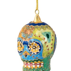 May include: A colourful, hand-painted ceramic ornament shaped like a skull. The ornament is decorated with intricate patterns in shades of blue, green, yellow, and pink. It has a gold loop for hanging.