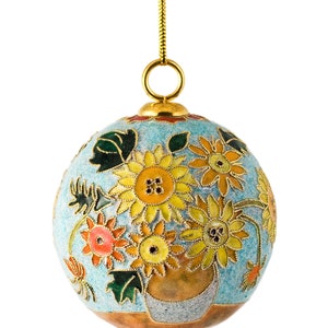 May include: A blue and gold Christmas ornament with a floral design. The ornament features a vase with sunflowers, daisies, and other flowers in shades of yellow, orange, and red.