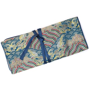 Pode incluir: Uma bolsa de tecido azul com um padrão de ondas douradas e vermelhas e um laço azul. A bolsa é feita de tecido brocado.