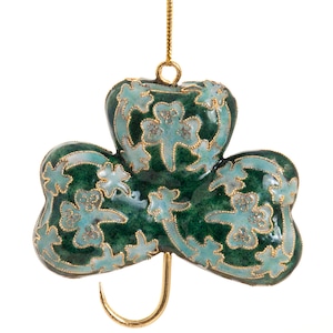 Puede incluir: Adorno de trébol verde y azul claro con ribete dorado y un lazo dorado para colgar. El trébol tiene un diseño floral detallado y está suspendido por un cordón dorado. Un artículo decorativo para el Día de San Patricio.